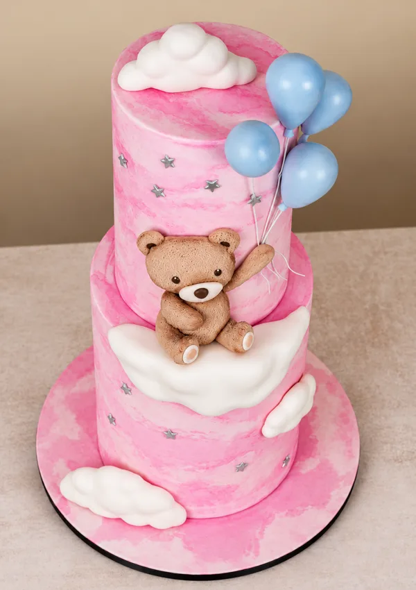 Torta de dos pisos rosa con nubes, globos y un osito