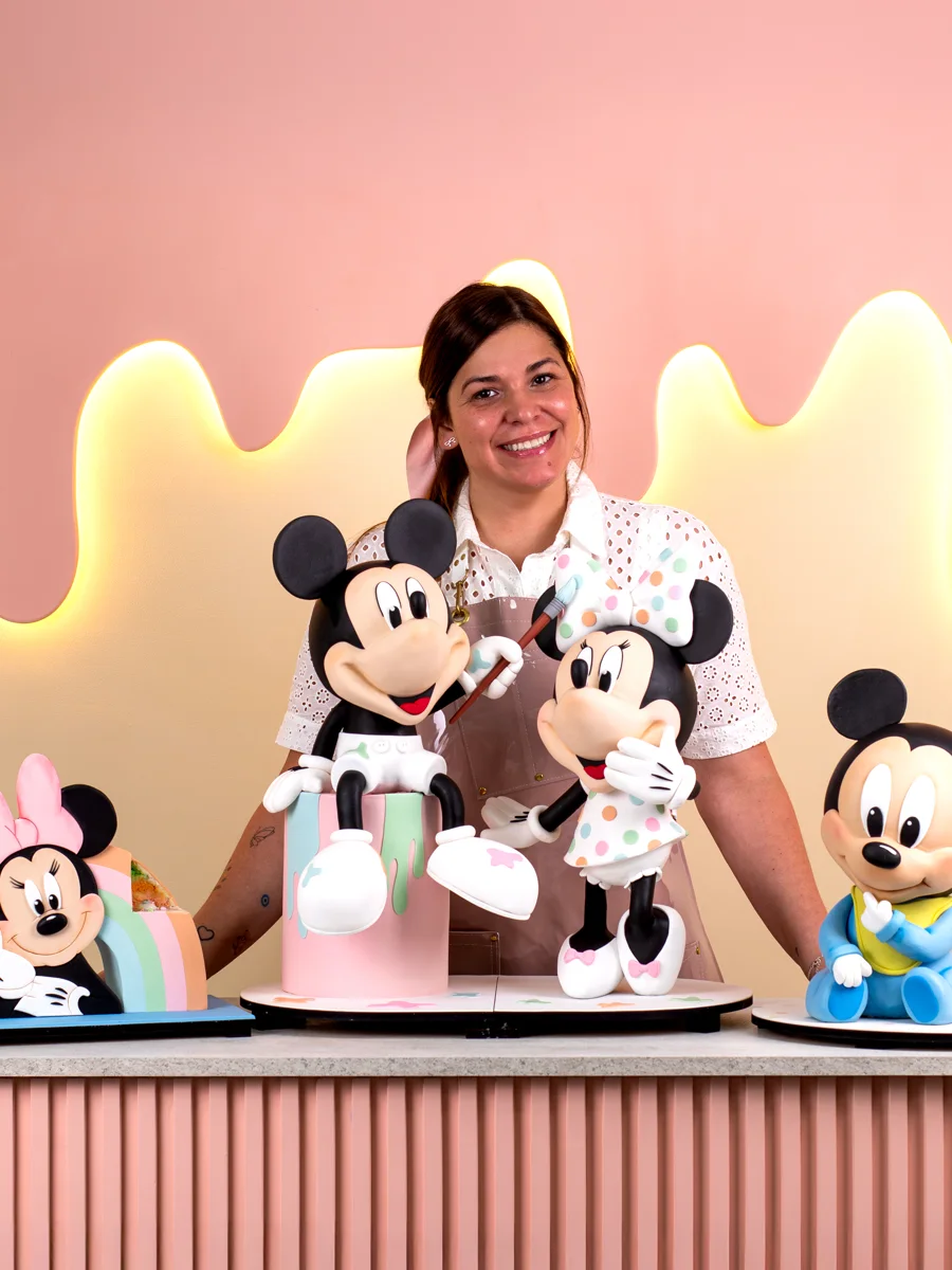 Pamela Pastor sonriendo detrás de sus tortas en estructura de Mickey, Minnie y Baby Mickey